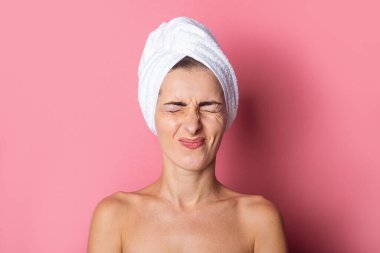 Kafasında havlu olan şaşı bir genç kadın, pembe arka planda sıkıca kapalı gözler..