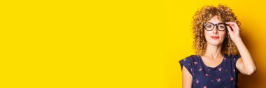 Sarı arka planda şeffaf gözlüklü, gülümseyen kıvırcık kadın. Pankart.