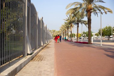 Birçok palmiye ağacı ve metal çit boyunca uzun kaldırım yolu 