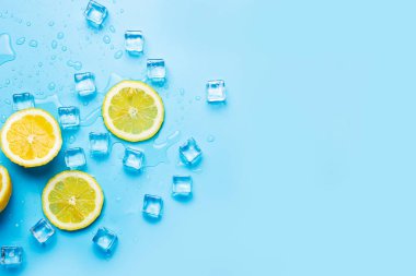 Mavi arka planda sulu taze limon dilimleri ve buz küpleri. Üst manzara, düz uzanma.