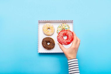 Kadın eli mavi arka planda donut tutuyor. Şekerleme dükkanı, hamur işleri, kahve dükkanı. Pankart. Düz yatış, üst görünüm.