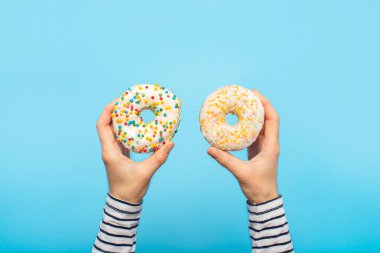 Dişi eller mavi arka planda donut tutarlar. Şekerleme dükkanı, hamur işleri, kahve dükkanı. Pankart. Düz yatış, üst görünüm.