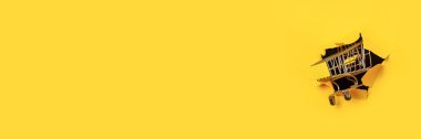 Sarı arka planda yırtık bir delikte boş bir alışveriş arabası. Alışveriş, online alışveriş, self servis. Pankart.