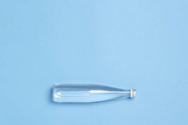 Mavi arka planda berrak su bulunan cam şişe. Sağlık ve güzellik kavramı, su dengesi, susuzluk, sıcaklık, yaz. Düz yatış, üst görünüm.