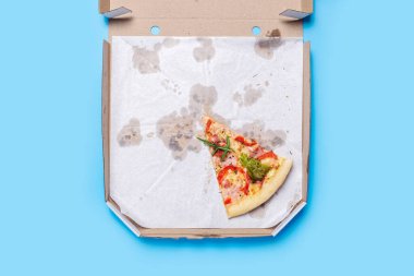 Bir dilim taze pizza mavi arka planda karton bir paketin içinde yatıyor. Üst manzara, düz uzanma. 