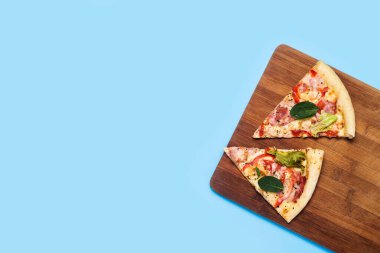 İki dilim taze pizza mavi arka planda, tahta bir tahtanın üzerinde yatıyor. Üst manzara, düz uzanma.