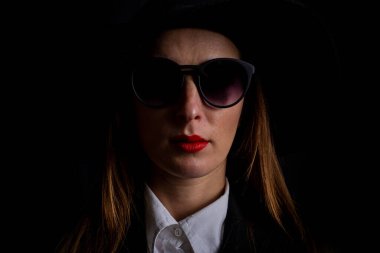 Siyah şapkalı güzel bir kadın ve siyah arka planda gözlüklü..