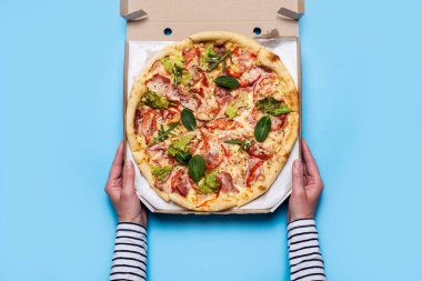 Kadın eli sarı arka planda bir paket pizza açar. Üst manzara, düz uzanma.