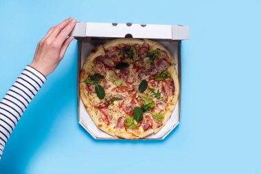 Kadın eli mavi arka planda bir paket pizza açıyor. Üst manzara, düz uzanma.