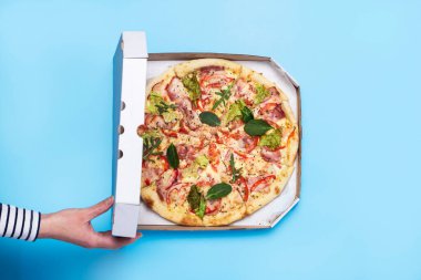 Kadın eli mavi arka planda bir paket pizza açıyor. Üst manzara, düz uzanma.
