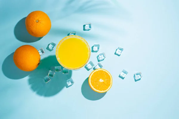 glass with orange cocktail, orange and ice cubes on a blue background. Top view, flat lay.