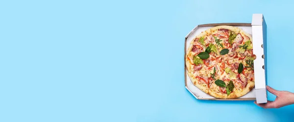 female hand open a package of pizza on a blue background. Top view, flat lay. Banner.