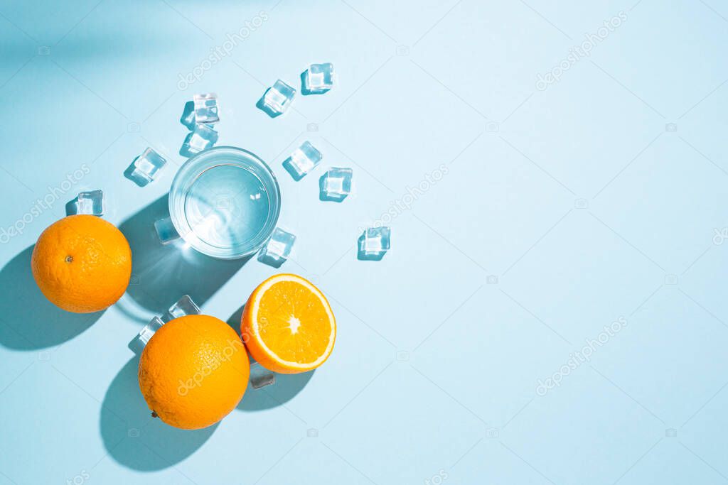 oranges, a glass of water and ice cubes on a table on a blue background. Top view, flat lay.