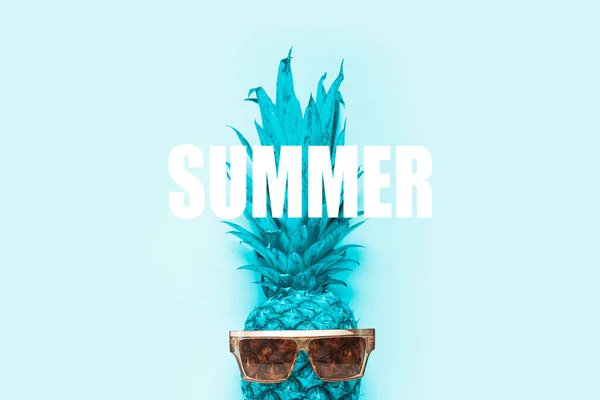 blue whole pineapple in sunglasses on a light blue background. Added the word Summer. Top view, flat lay.