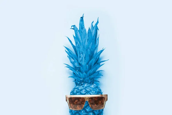 blue whole pineapple in sunglasses on a light blue background. Top view, flat lay.