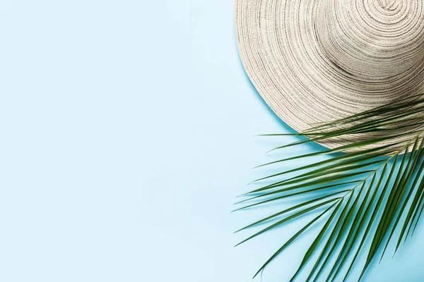 Women\'s hat with wide brim and a branch of a palm tree on a blue background. Summer concept, vacation at sea. Banner. Flat lay, top view.