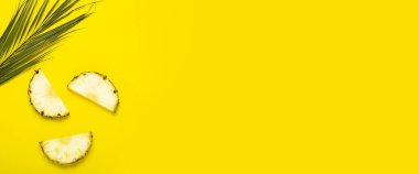 Olgun ananas dilimleri, yapraklı ananas ve sarı arka planda bir palmiye yaprağı. Üst manzara, düz uzanma.