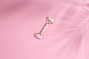 Beyaz doğal kuvars yüz silindiri, pembe arka planda palmiye yaprağı gölgesi. Üst manzara, düz uzanma. 