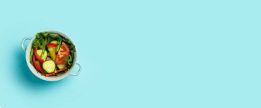 Açık mavi arka planda mavi bir kasede sebze salatası. Üst manzara, düz yatış. Pankart.