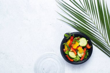 Plastik bir kasede sebze salatası ve biton arka planda yeşil bir palmiye yaprağı.. 