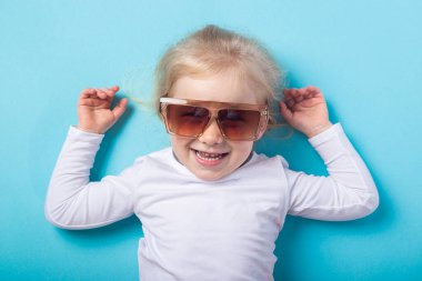 Güneş gözlüklü güzel sarışın kız mavi arka planda yatıyor. Üst manzara, düz uzanma.