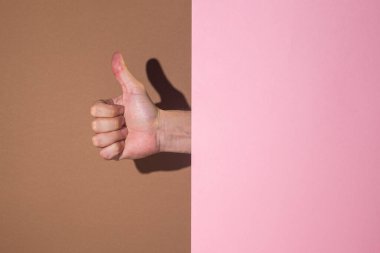 Kadın eli, kahverengi arka planda karton pembe arka planda boşluk boyunca başparmaklarını gösteriyor..
