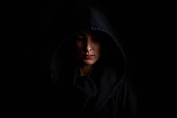 Young woman in a black hood on a dark black background.