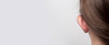 Hafif bir arka planda, sarkık kulaklı kadın dikiz aynası. Otoplasti, kulakçık plastiği. Pankart. 