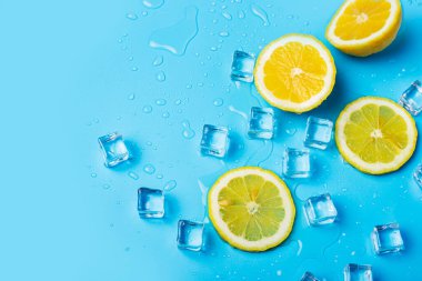 Mavi arka planda sulu taze limon dilimleri ve buz küpleri. Üst manzara, düz uzanma.