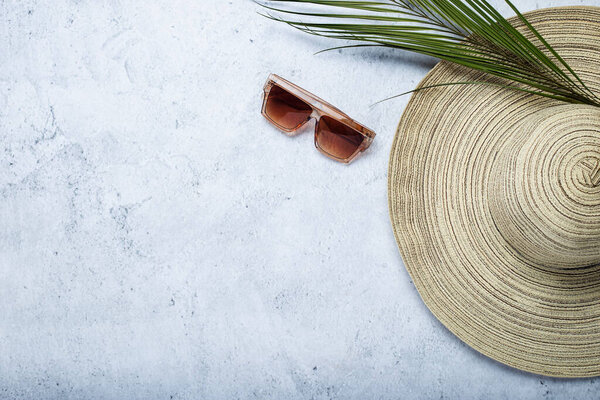 Women's hat, sunglasses and a leaf of a palm tree on a concrete background. Top view, flat lay.