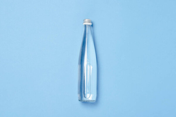 Стеклянная бутылка с чистой водой на синем фоне. Концепция здоровья и красоты, водный баланс, жажда, жара, лето. Плоский, вид сверху.