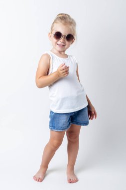 Güneş gözlüklü sarışın çocuk stüdyoda arka planda poz veriyor..