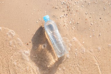 Plajdaki plastik su şişesi bir dalga tarafından yıkanır. Üst manzara, düz uzanma. 