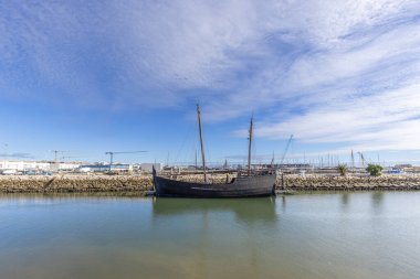 Lagos, Algarve, Portekiz 'deki marinaya demirlemiş geleneksel ahşap yelkenli gemisi parlak mavi gökyüzünün altındaki durgun suya yansıyor..