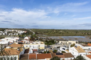 Castro Marim 'in geniş panoramik manzarası, Portekiz' in Algarve bölgesindeki parlak gökyüzü altında kırmızı çatıları, sokakları ve çevresindeki kırsal alanları olan geleneksel beyaz evleri gösteriyor..