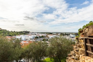 Castro Marim 'in geniş panoramik manzarası, Portekiz' in Algarve bölgesindeki parlak gökyüzü altında kırmızı çatıları, sokakları ve çevresindeki kırsal alanları olan geleneksel beyaz evleri gösteriyor..