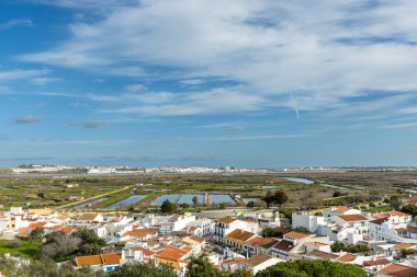 Castro Marim 'in geniş panoramik manzarası, Portekiz' in Algarve bölgesindeki parlak gökyüzü altında kırmızı çatıları, sokakları ve çevresindeki kırsal alanları olan geleneksel beyaz evleri gösteriyor..