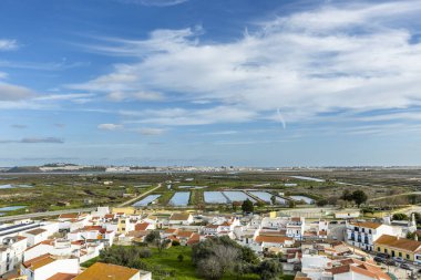 Castro Marim 'in geniş panoramik manzarası, Portekiz' in Algarve bölgesindeki parlak gökyüzü altında kırmızı çatıları, sokakları ve çevresindeki kırsal alanları olan geleneksel beyaz evleri gösteriyor..