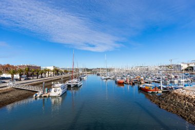Lagos, Algarve, Portekiz 'deki marinanın güneşli manzarasında, arka planda modern liman binaları bulunan çok sayıda yat ve tekne yer alıyor..