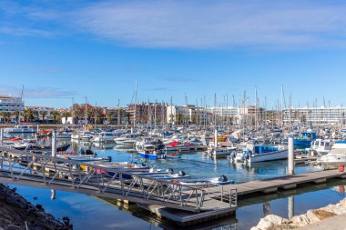 Lagos, Algarve, Portekiz 'deki marinanın güneşli manzarasında, arka planda modern liman binaları bulunan çok sayıda yat ve tekne yer alıyor..