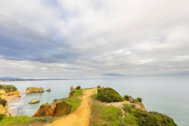 Lagos, Algarve, Portekiz 'deki Atlantik Okyanusu üzerinde sakin mavi sulara bakan yemyeşil çimenler ve dramatik sahil kayalıkları ile huzurlu bir manzara..