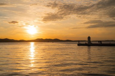 Hırvatistan 'ın Zadar kentinde deniz feneri simgesiyle deniz kenarında güzel bir gün batımı.