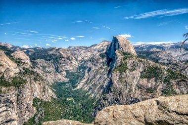 Ortasında büyük bir tepe olan bir dağ sırası. Gökyüzü açık ve mavi. Dağ sırası ağaçlarla kaplı ve tepe de karla kaplı.