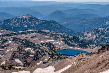Ortasında göl olan bir dağ sırası. Göl ağaçlarla çevrilidir ve dağlar karla kaplıdır. Huzurlu ve huzurlu bir sahne.