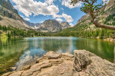 Dağlarla çevrili güzel bir göl. Gökyüzü mavi ve bulutlar beyaz. Göl sakin ve huzurlu.