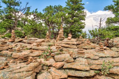 Birkaç ağacı ve birkaç küçük kaya yığını olan kayalık bir yamaç. Kayalar daha büyük bir yapının parçasıymış gibi görünecek şekilde istiflenmiş. Sahnenin huzurlu ve huzurlu bir havası var.
