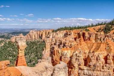 Önünde büyük bir kaya oluşumu olan güzel bir dağ sırası. Gökyüzü açık ve mavi, ve arkadaki ağaçlar yemyeşil ve yemyeşil