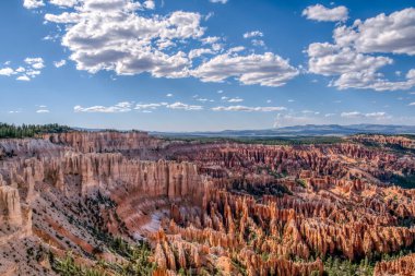 Açık mavi gökyüzü olan güzel, kayalık bir manzara. Dağlar ağaçlarla örtülmüş, gök de bulutlarla örtülmüştür. Manzara, dağların engin genişliğiyle huzurlu ve huzurlu.