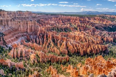 Önünde ağaçlar olan kırmızı kaya oluşumlarından oluşan güzel bir manzara. Gökyüzü mavi ve güneş parlıyor.