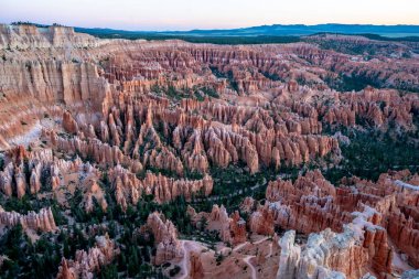Birçok kırmızı kaya oluşumuna sahip bir kanyonun panoramik görüntüsü. Gökyüzü pembe ve güneş batıyor.